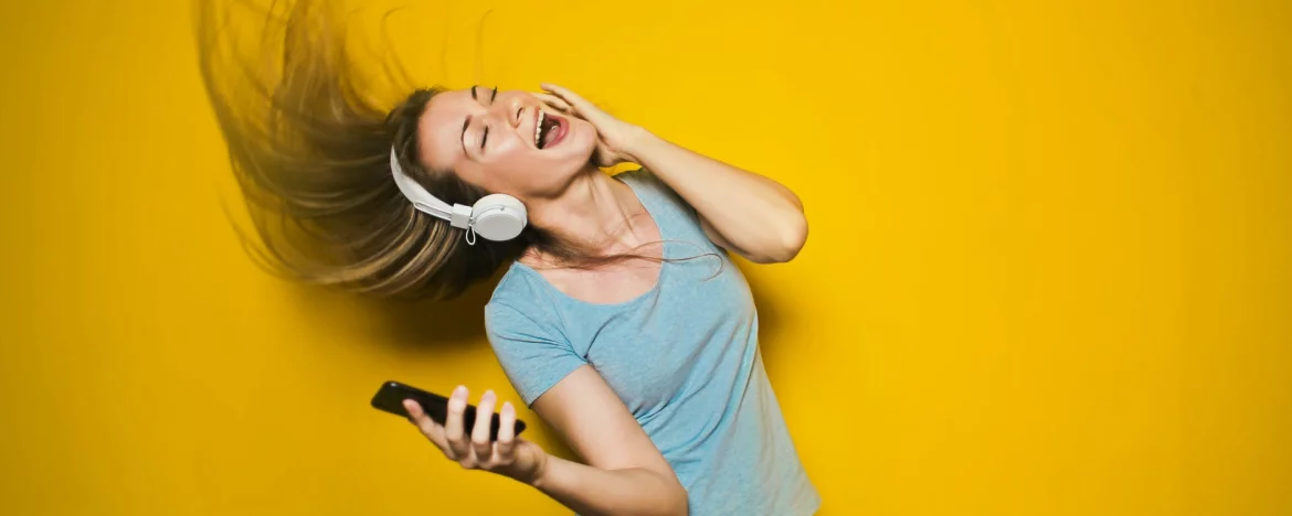 Woman enjoying listening to music on headphones with yellow background.