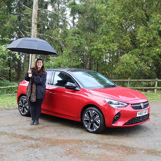 woman with umbrella next to Corsa-e